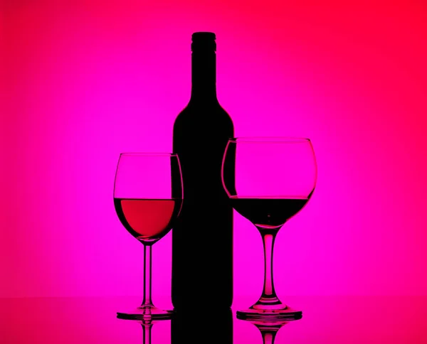Twee gevulde glazen met rode wijn en sherry, zwart flessensilhouet op een gespiegelde achtergrond in de zijde roze en paarse verlichting. Concept verkoop, korting prijs. — Stockfoto