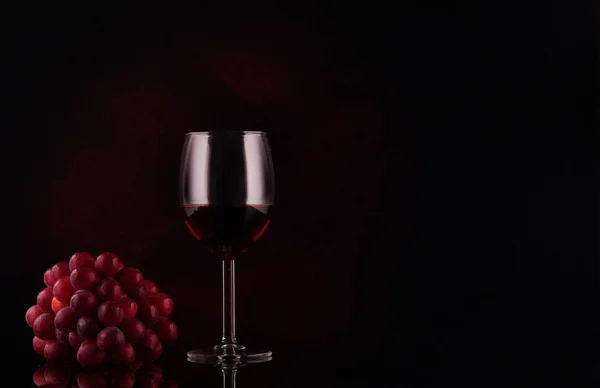 Kleine tak van druiven en glas met wijn op zwarte achtergrond met reflecties en kopieerruimte. — Stockfoto