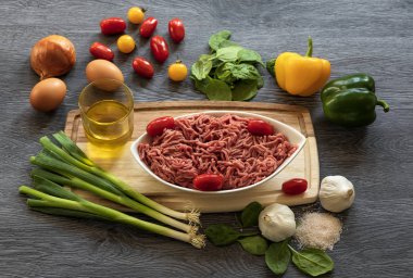 Beyaz bir tabakta kıyma. Ispanak yaprakları, sarımsak, kırmızı ve sarı domates, ahşap zemin üzerinde soğan