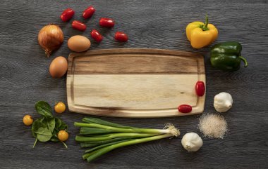 Metin için kopyalama alanı olan ahşap bir yemek tahtası ıspanak yaprakları, kırmızı ve sarı domates, pembe deniz tuzu, sarımsak, biber ve soğan. Koyu ahşap arka plan. Üst görünüm
