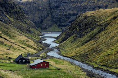 Kırmızı ve siyah evler inanılmaz yeşil bir vadide duruyor. Saksun 'un küçük bir köyünde sonbahar. Streymoy, Faroe Adaları. Avrupa