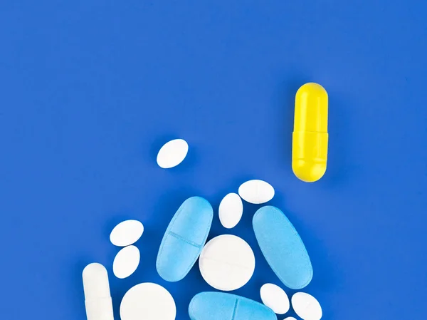Comprimidos, comprimidos e cápsulas de medicamentos variados sobre fundo azul — Fotografia de Stock