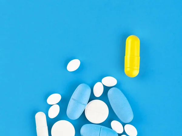 Comprimidos, comprimidos e cápsulas de medicamentos variados sobre fundo azul — Fotografia de Stock