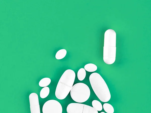 Comprimidos, comprimidos e cápsulas de medicamentos variados em fundo verde — Fotografia de Stock