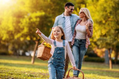 Gülümseyen aile parkta piknik yapıyor. Doğaları gereği eğleniyorlar. Aşk, doğa ve mutluluk kavramı..