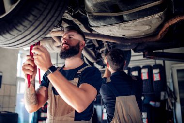 Servis merkezinde araba tamir eden iki tamirci.