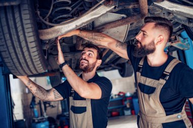 Servis merkezinde araba tamir eden iki tamirci.