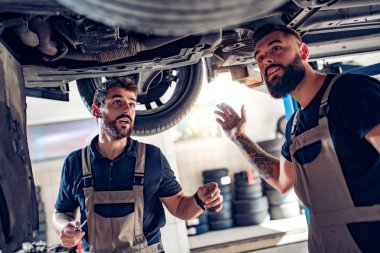 Servis merkezinde araba tamir eden iki tamirci.