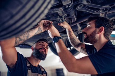 Servis merkezinde araba tamir eden iki tamirci.