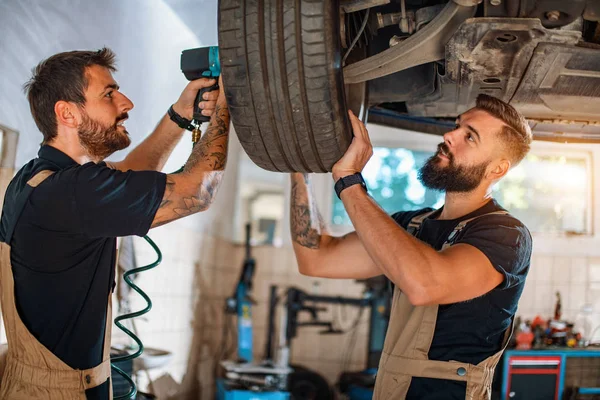 Servis merkezinde araba tamir eden iki tamirci.