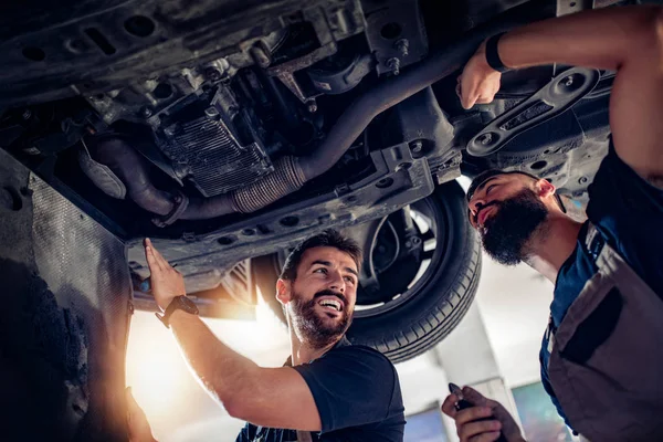 Dwóch mechaników naprawiających samochód w centrum serwisowym — Zdjęcie stockowe