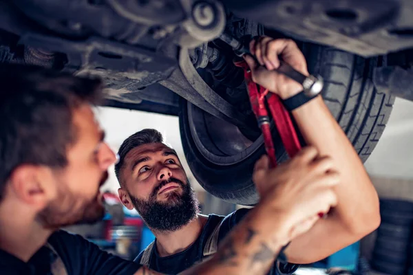 Jovens mecânicos mudar roda de carro na oficina de reparação de automóveis — Fotografia de Stock