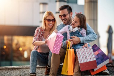 Alışveriş torbalarıyla mutlu bir aile. Aile alışverişi. Genç ebeveynler ve kızları alışveriş torbaları taşıyor. Alışveriş sonrası dinlenen mutlu bir aile..