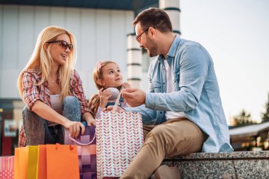 Alışveriş torbalarıyla mutlu bir aile. Aile alışverişi. Genç ebeveynler ve kızları alışveriş torbaları taşıyor. Alışveriş sonrası dinlenen mutlu bir aile..