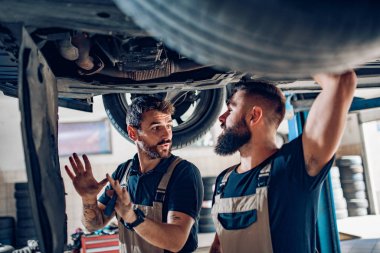 Üniformalı iki teknisyen otomobil servisinde çalışıyor. İletişim kontrolü ve onarım. Araba atölyesinde takım çalışması konsepti..