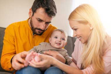 Genç ebeveynler ve onların küçük tatlı oğulları sofast 'ta dinleniyorlar. Mutlu anne, baba ve bebek evde. Küçük bir oğlu olan güzel genç bir çift..