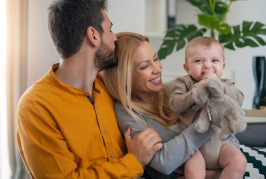 Genç ebeveynler ve onların küçük tatlı oğulları sofast 'ta dinleniyorlar. Mutlu anne, baba ve bebek evde. Küçük bir oğlu olan güzel genç bir çift..