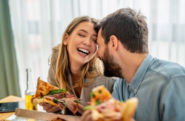 Genç çiftin evde pizza yerken çekilmiş yakın bir fotoğrafı. Çift öğle yemeğinde pizza yiyor. İnsanlar, aşk, yemek ve mutluluk konsepti..