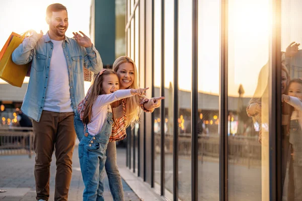 Mutlu genç ebeveynler ve kızları alışveriş torbaları tutuyor ve alışveriş sonrası gülümsüyorlar..
