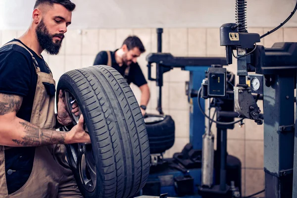 Teamwork.Mechanic holding a tire at the repair garage. Replacement of winter and summer tires.