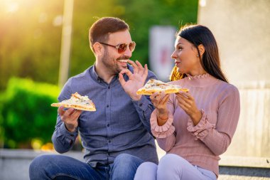 Açık havada pizza yiyen mutlu genç bir çift fotoğrafı. Fast food konsepti..