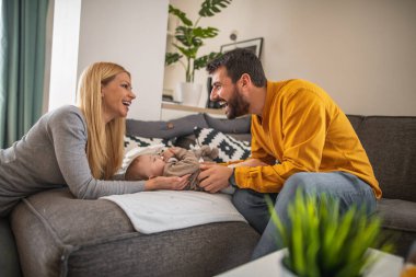 Genç ebeveynler ve onların küçük tatlı oğulları sofast 'ta dinleniyorlar. Mutlu anne, baba ve bebek evde. Küçük bir oğlu olan güzel genç bir çift..