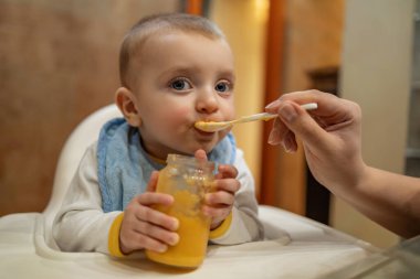 Evde püre ve kaşıkla bebek besleyen bir anne. Aile, sevgi, yemek ve sağlıklı yaşam tarzı kavramı..