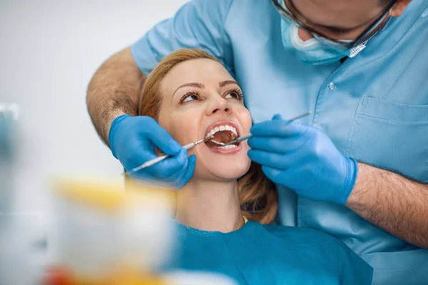 Diş hekiminde tedavi gören kadın hasta portresi. Diş hekiminde hastanın dişlerini muayene eden diş hekimi..
