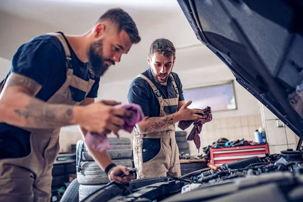 Young mechanics change oil and pour new oil into the car engine  in vehicle workshop.