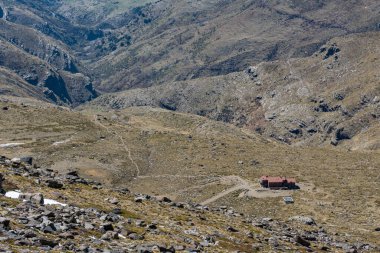 Helikopter pisti olan yüksek dağ sığınağı ve arka planda hava manzaralı bir vadi.