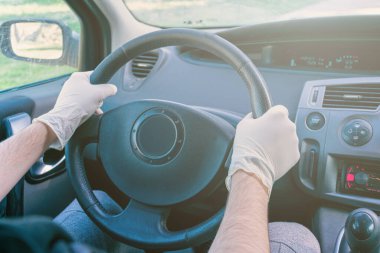 Salgından korunmak için eldiven takıp direksiyonu tutan eller.