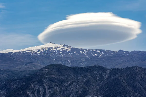 Sierra Nevada 'da Pico del Caballo adında karlı bir dağın tepesinde mercek bulutu.