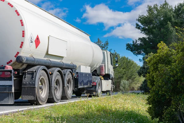 Yakıt tankı kamyonu ağaçlık bir yolda gidiyor.