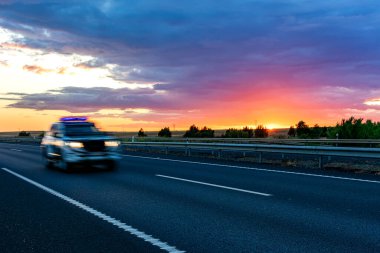 Otoyolda yüksek hızda giden polis arabası ufukta dramatik bir günbatımı gökyüzü belirdi.
