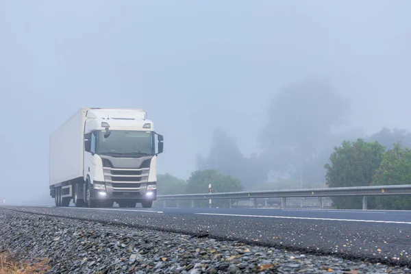 Truck with refrigerated semi-trailer driving on the highway on a thick foggy day