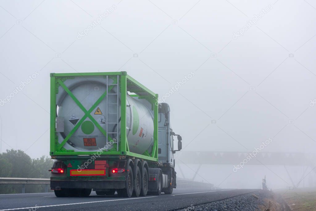 Truck transporting container with dangerous goods circulating on a highway with dense fog