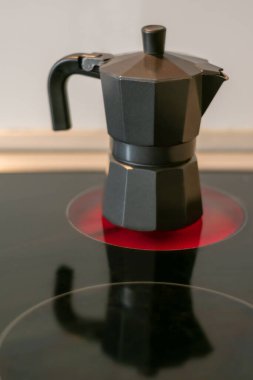 Bardakta yansıması olan seramik bir hob ateşinde kahve makinesi.