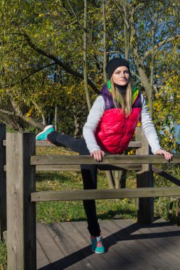 Güzel bir kız bir ince rakam siyah tayt ve parlak pembe ceket ile güneşli havalarda sonbahar parkta spor oynuyor.