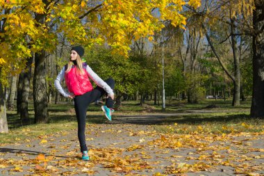 Güzel bir kız bir ince rakam siyah tayt ve parlak pembe ceket ile güneşli havalarda sonbahar parkta spor oynuyor.