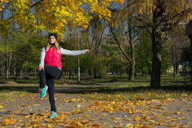 Güzel bir kız bir ince rakam siyah tayt ve parlak pembe ceket ile güneşli havalarda sonbahar parkta spor oynuyor.