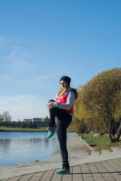 Güzel bir kız bir ince rakam siyah tayt ve parlak pembe ceket ile güneşli havalarda sonbahar parkta spor oynuyor.