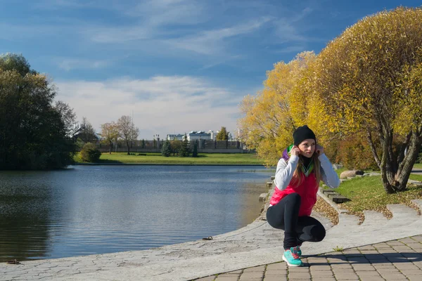 Güzel bir kız bir ince rakam siyah tayt ve parlak pembe ceket ile güneşli havalarda sonbahar parkta spor oynuyor.