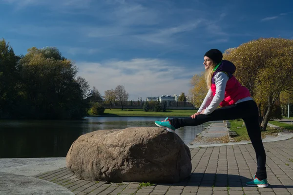 Güzel bir kız bir ince rakam siyah tayt ve parlak pembe ceket ile güneşli havalarda sonbahar parkta spor oynuyor.