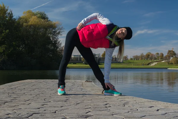 Güzel bir kız bir ince rakam siyah tayt ve parlak pembe ceket ile güneşli havalarda sonbahar parkta spor oynuyor.