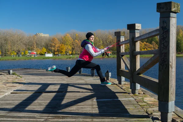 Güzel bir kız bir ince rakam siyah tayt ve parlak pembe ceket ile güneşli havalarda sonbahar parkta spor oynuyor.
