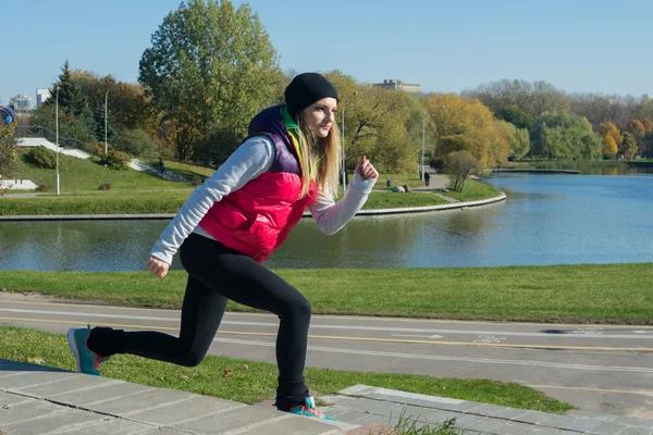 Uma menina bonita com uma figura fina nas leggings pretas e jaqueta rosa brilhante está jogando esportes no parque de outono em tempo ensolarado . — Fotografia de Stock