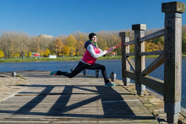Güzel bir kız bir ince rakam siyah tayt ve parlak pembe ceket ile güneşli havalarda sonbahar parkta spor oynuyor.