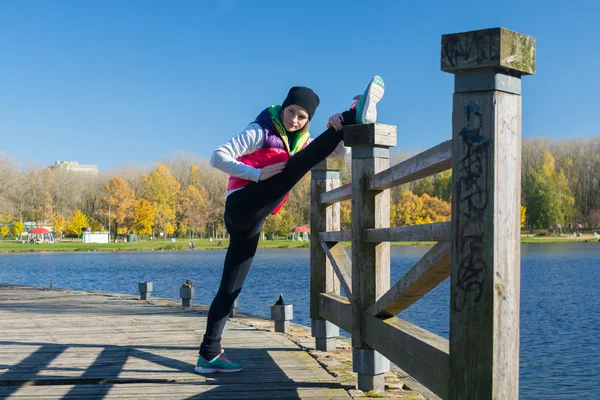 Güzel bir kız bir ince rakam siyah tayt ve parlak pembe ceket ile güneşli havalarda sonbahar parkta spor oynuyor.