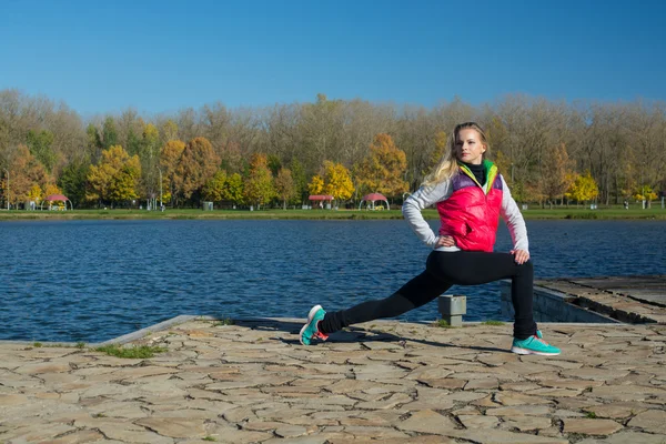 Güzel bir kız bir ince rakam siyah tayt ve parlak pembe ceket ile güneşli havalarda sonbahar parkta spor oynuyor.