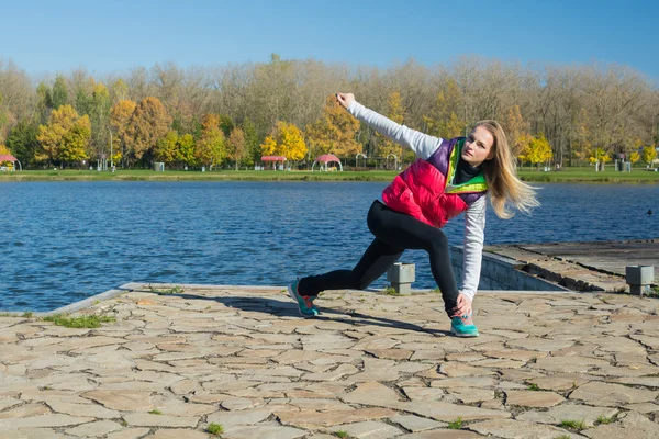 Güzel bir kız bir ince rakam siyah tayt ve parlak pembe ceket ile güneşli havalarda sonbahar parkta spor oynuyor.